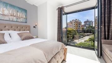 Een moderne slaapkamer met een groot bed, uitzicht op de stad door middel van kamerhoge ramen en een schilderij aan de muur.