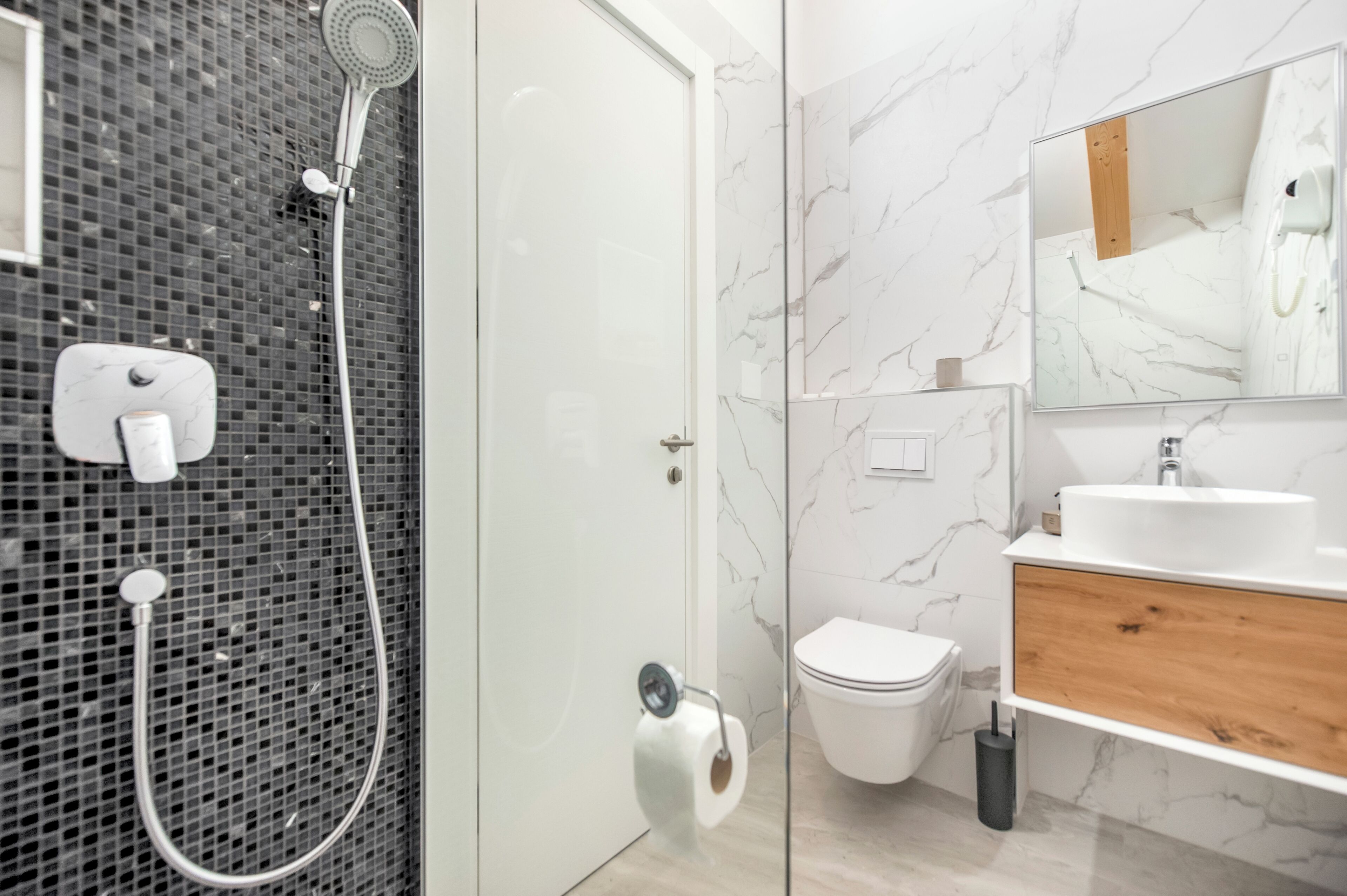 A modern bathroom with a glass-enclosed shower, a white toilet, a wooden vanity, and a marble backsplash.