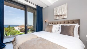 A bedroom with a large bed, a view of the sea, and a sailboat painting on the wall. - Boutique Residence Arion (Rovinj)