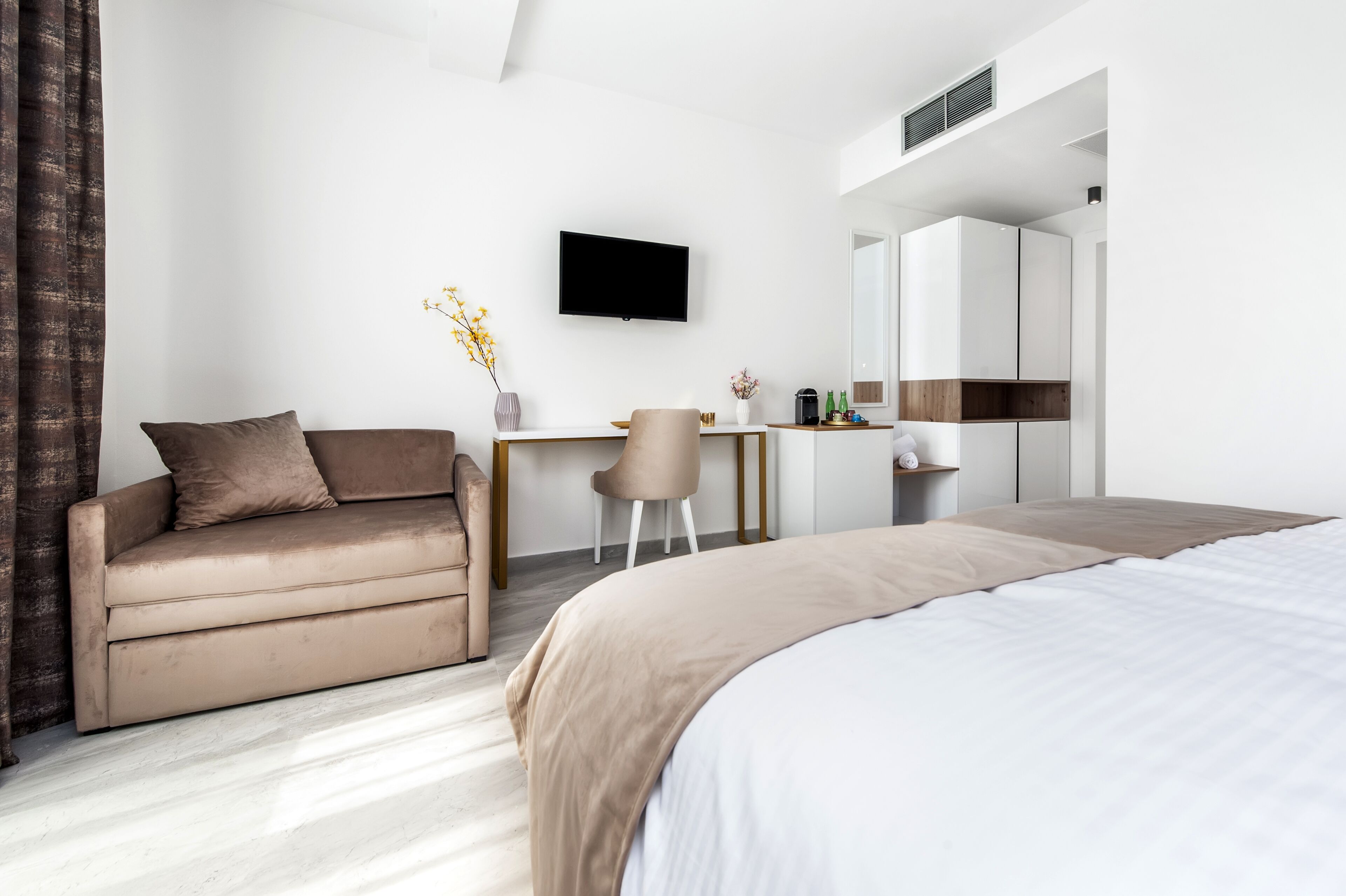 A modern hotel room with a bed, a sofa, a desk, and a TV.