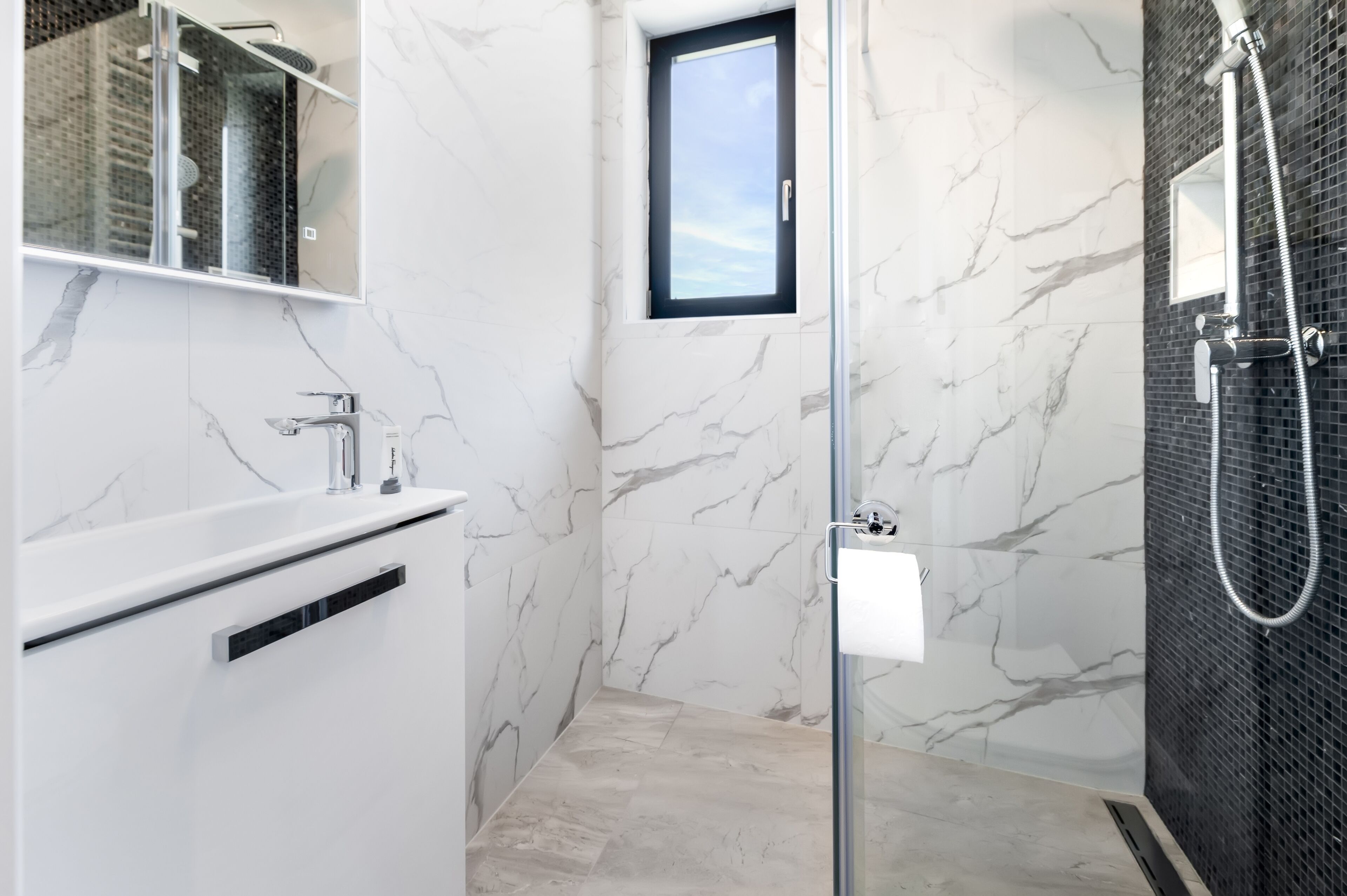 A modern bathroom with a glass-enclosed shower, a white vanity, and marble walls.