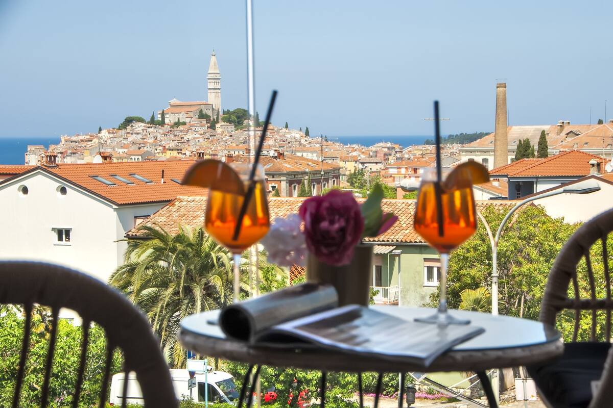 A table with a menu and two drinks, overlooking a coastal cityscape with historic buildings and a prominent tower.