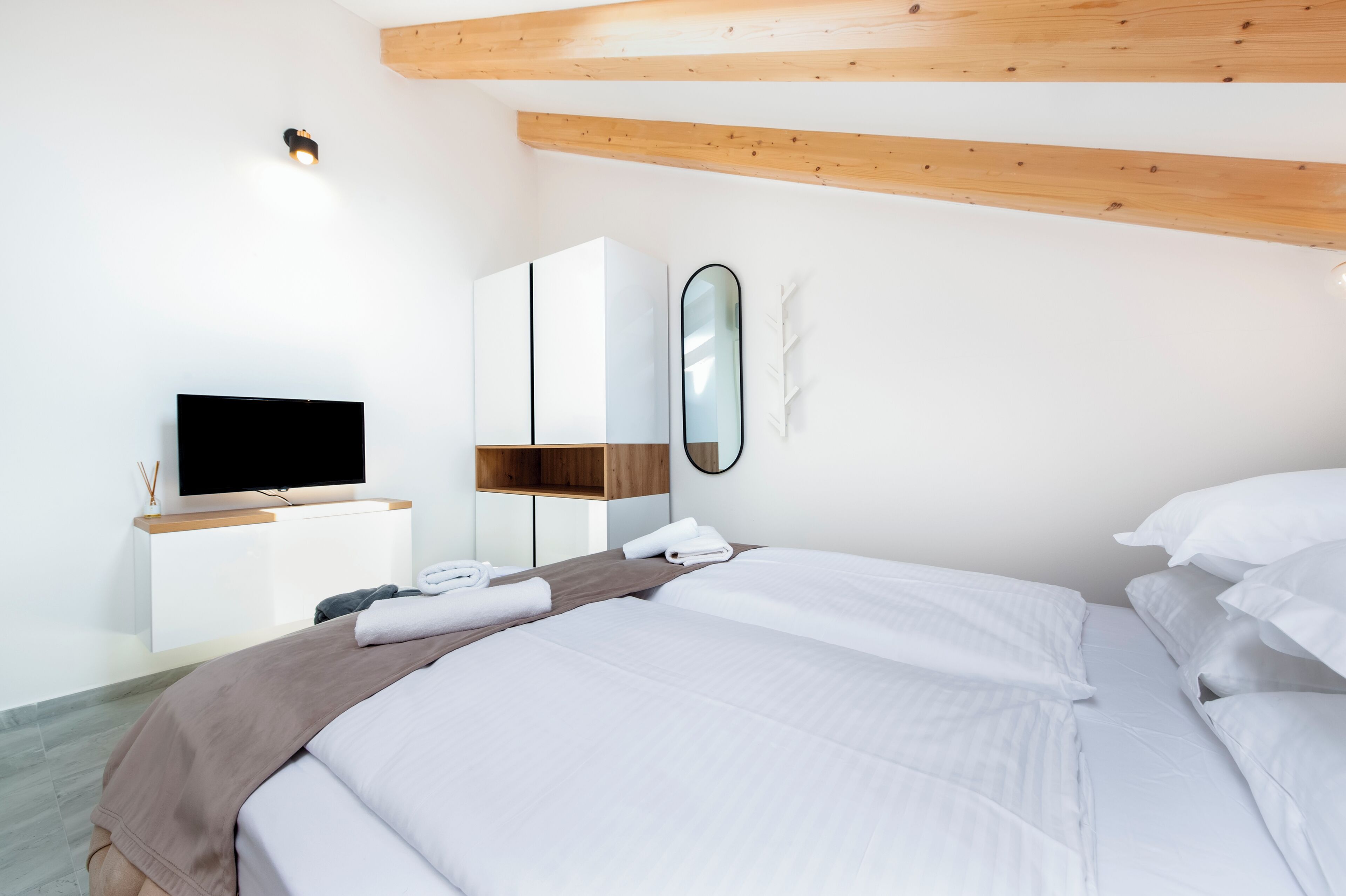 A modern hotel room with a large bed, a flat-screen TV, a wooden ceiling, and a white wardrobe.