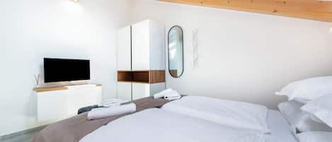 Una habitación de hotel moderna con una cama grande, un televisor de pantalla plana, techo de madera y un armario blanco.
