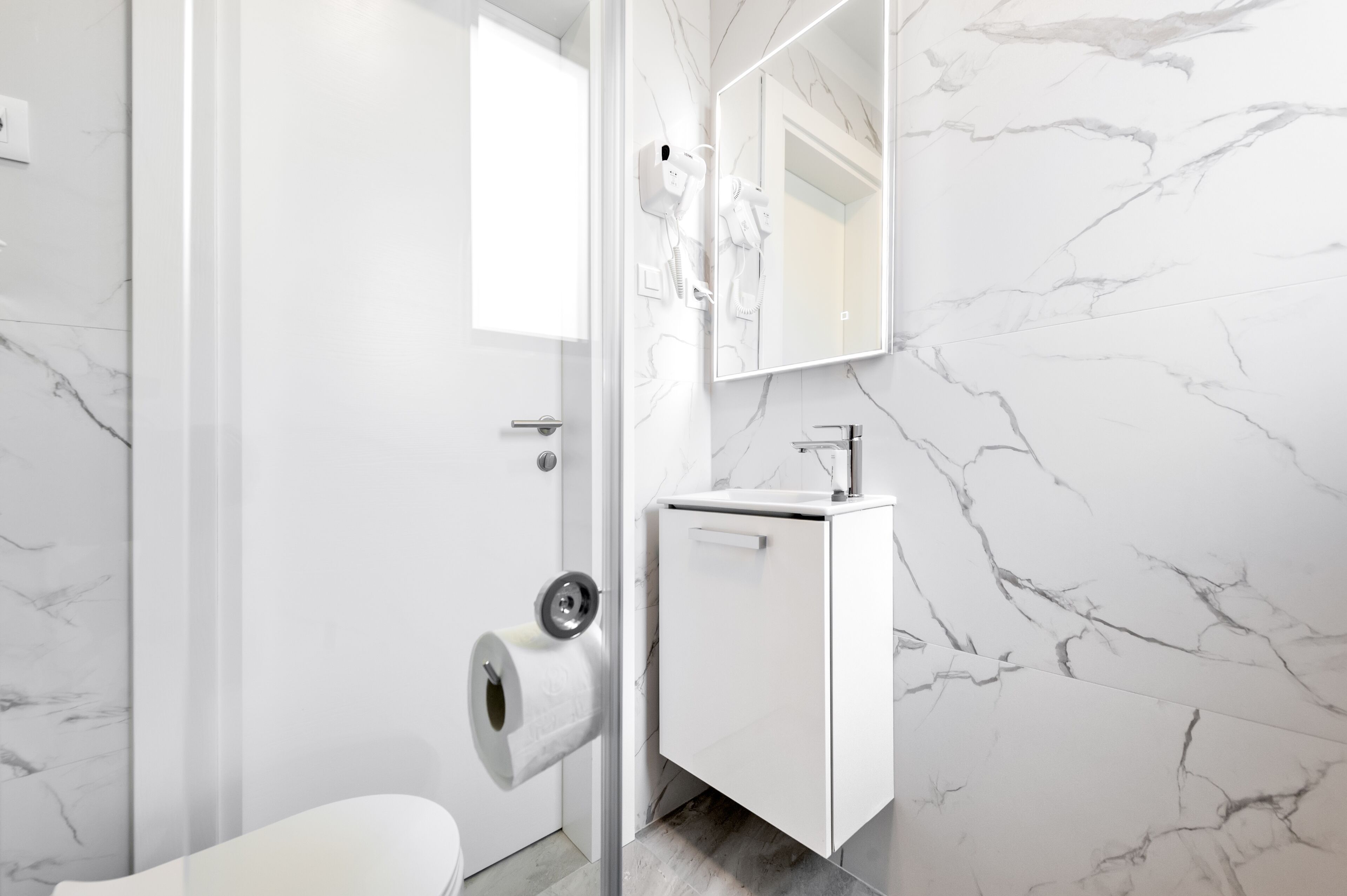 Une salle de bain avec un mur en marbre, un porte-rouleau de papier toilette, un lavabo et un miroir.