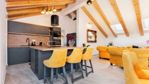 A modern kitchen with a central island, bar stools, and a dining area with yellow sofas. - Boutique Residence Arion (Rovinj)