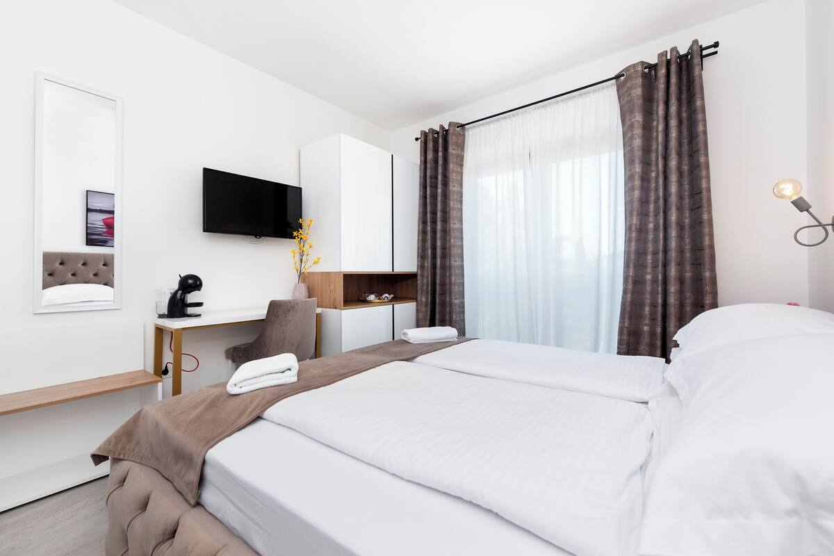 A hotel room with a bed, desk, chair, TV, and curtains.