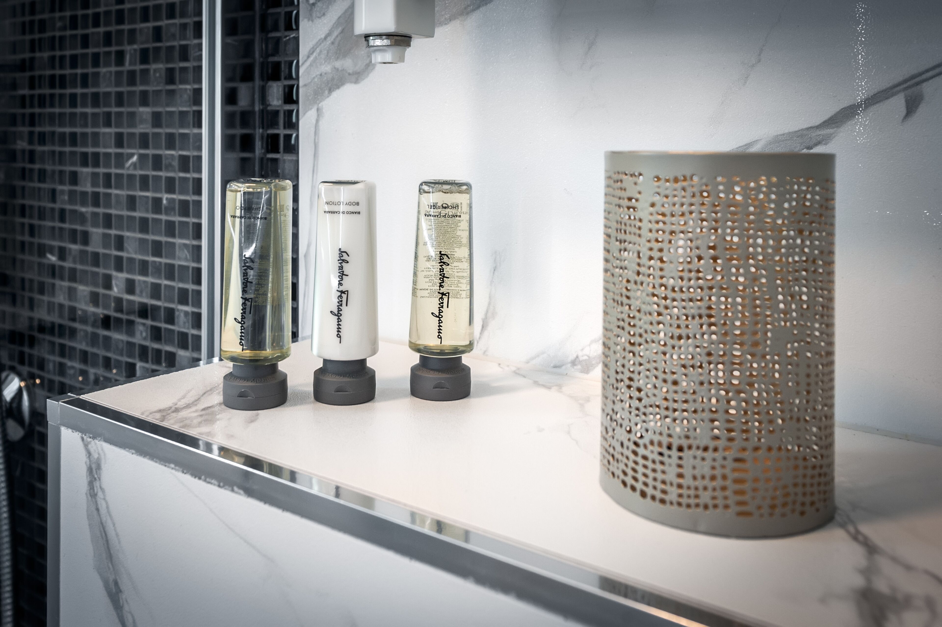 Three bottles of hair care product on a marble countertop next to a perforated vase.