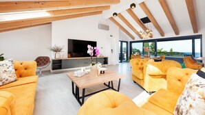 A spacious living area with yellow sofas, a wooden ceiling, and a large TV. - Boutique Residence Arion (Rovinj)
