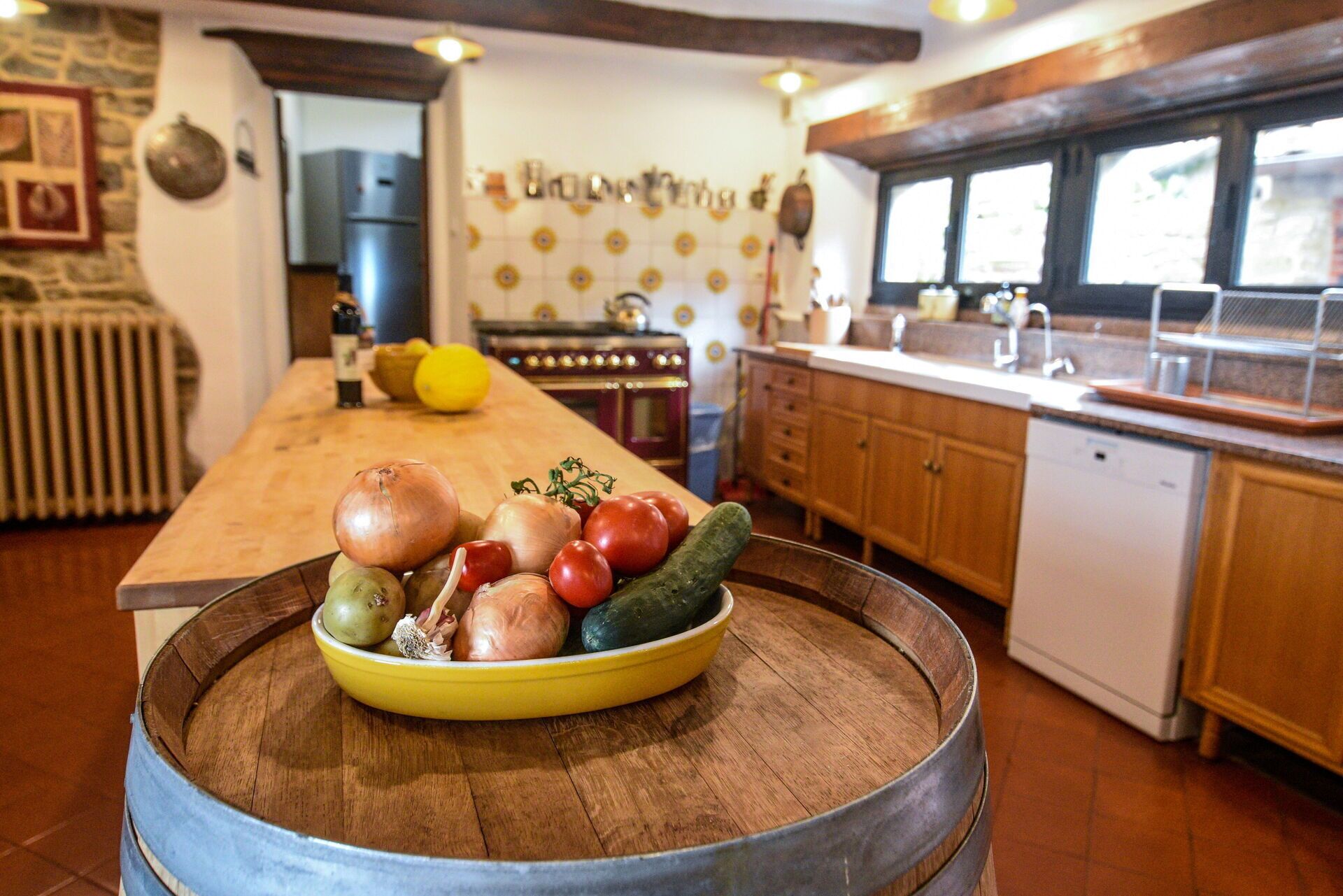 Una cocina con un barril de madera, un tazón amarillo de verduras y una estufa antigua.