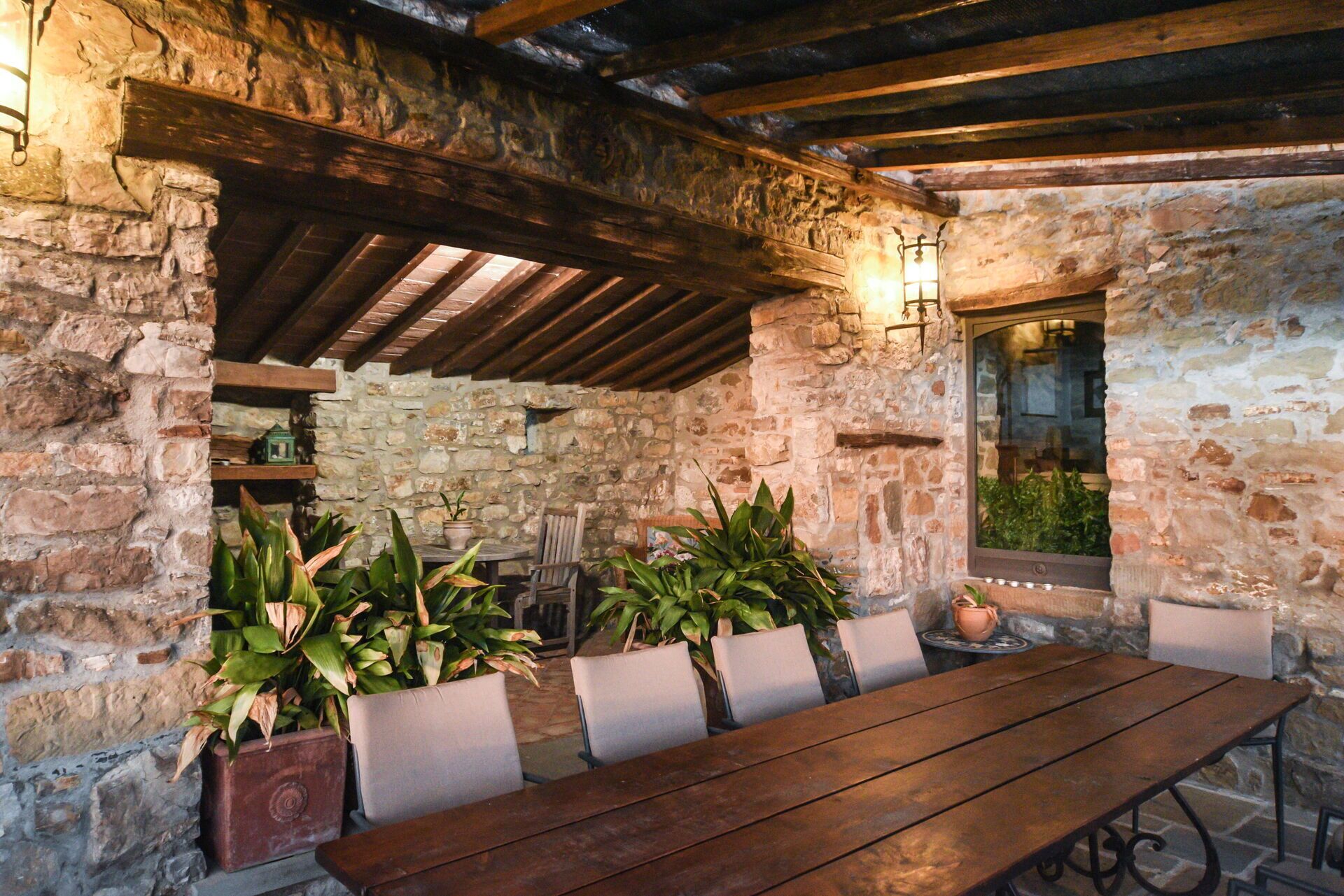 An outdoor dining area with stone walls, wooden beams, and potted plants.