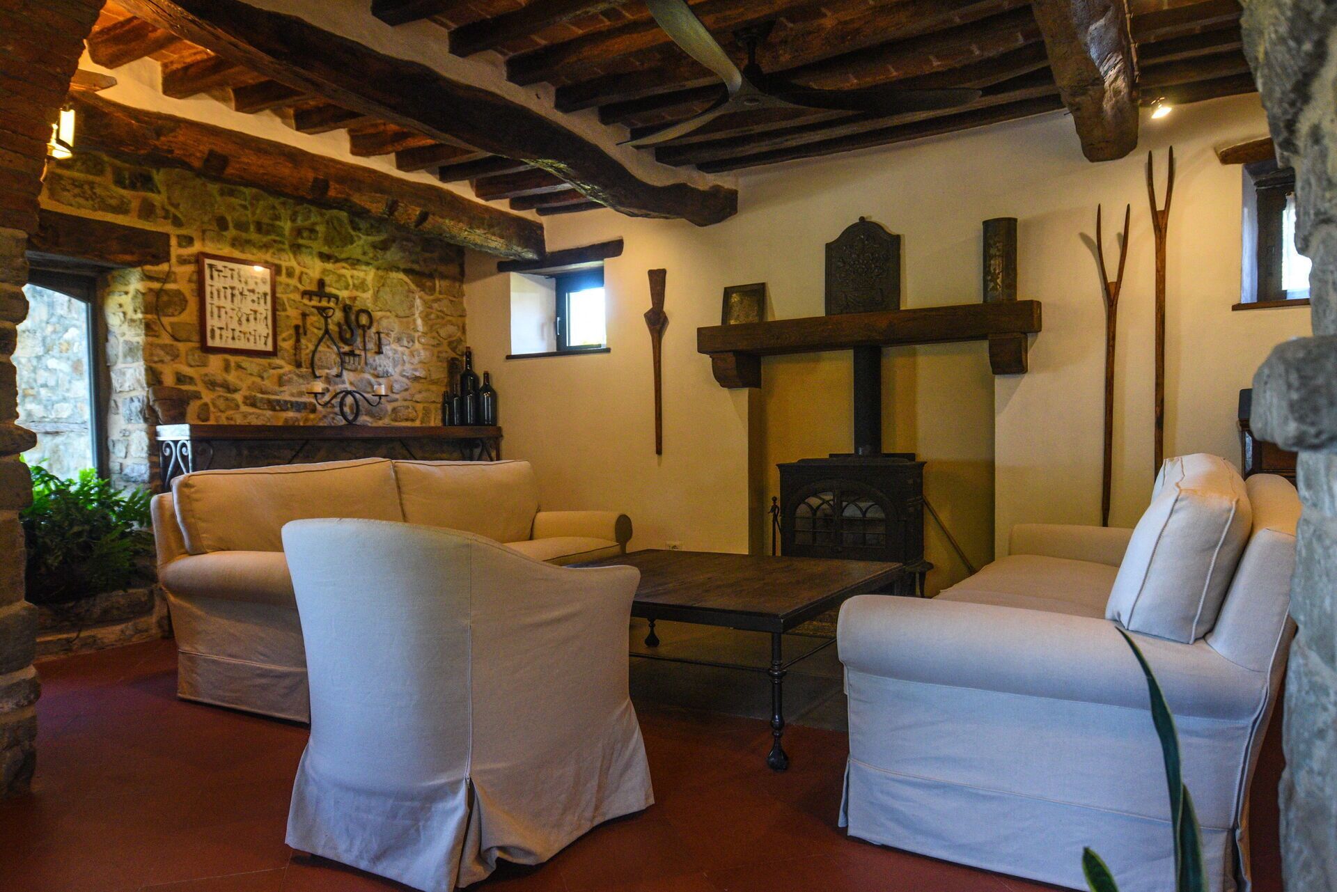 Una habitación acogedora con paredes de piedra, vigas de madera y chimenea. Hay dos sillones blancos y una mesita.