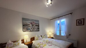 Ein Schlafzimmer mit zwei Betten, einem Bild von einem Fahrrad, einem Fenster mit Vorhängen und einer Heizung.