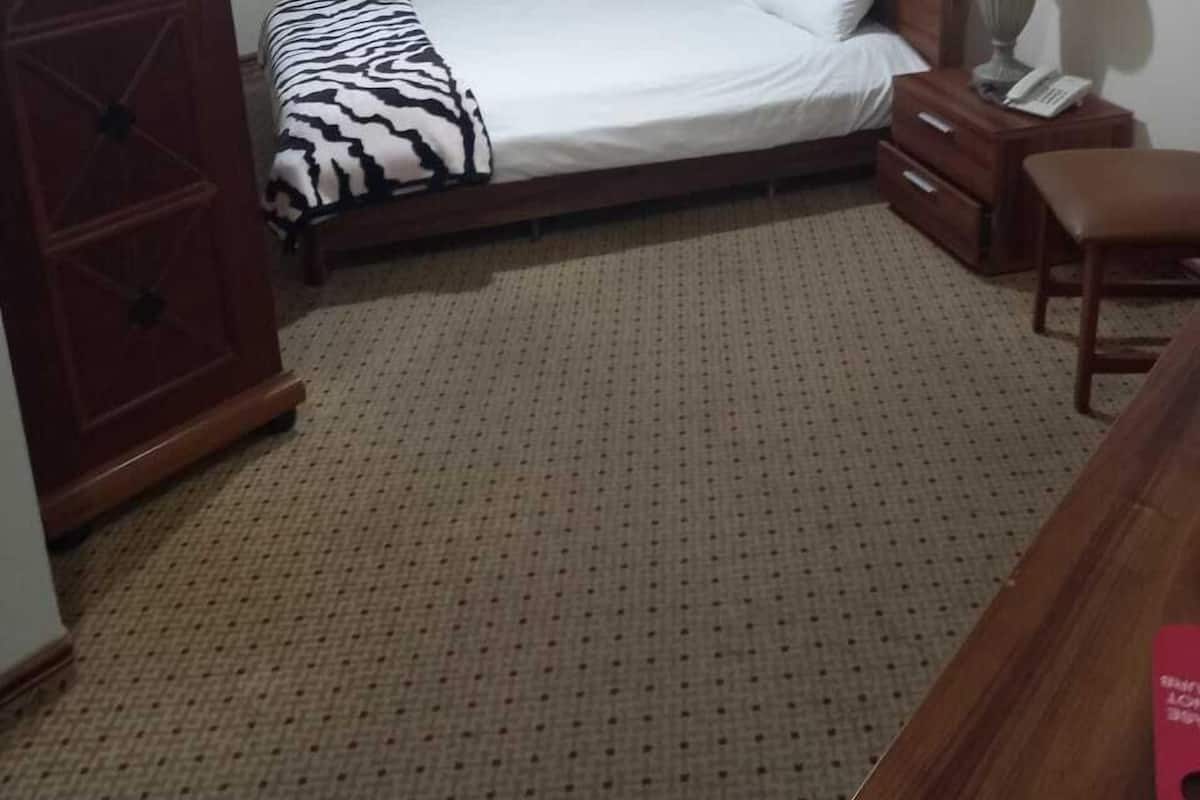 A bedroom with a bed, wooden wardrobe, bedside table, lamp, and a small desk.