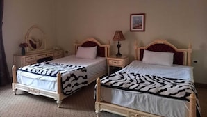A hotel room with two beds, each with a zebra-patterned bedspread, a bedside table with a lamp, and a mirror on the dresser.