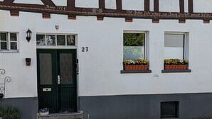 Ein traditionelles Fachwerkhäuschen mit einer dunkelgrünen Tür, Hausnummer 27, und Blumenkästen an den Fensterbänken.