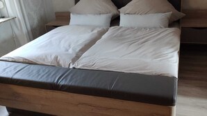 Ein Bett mit Holzgestell, grauem Lattenrost, zwei Kissen und einem Nachttisch.