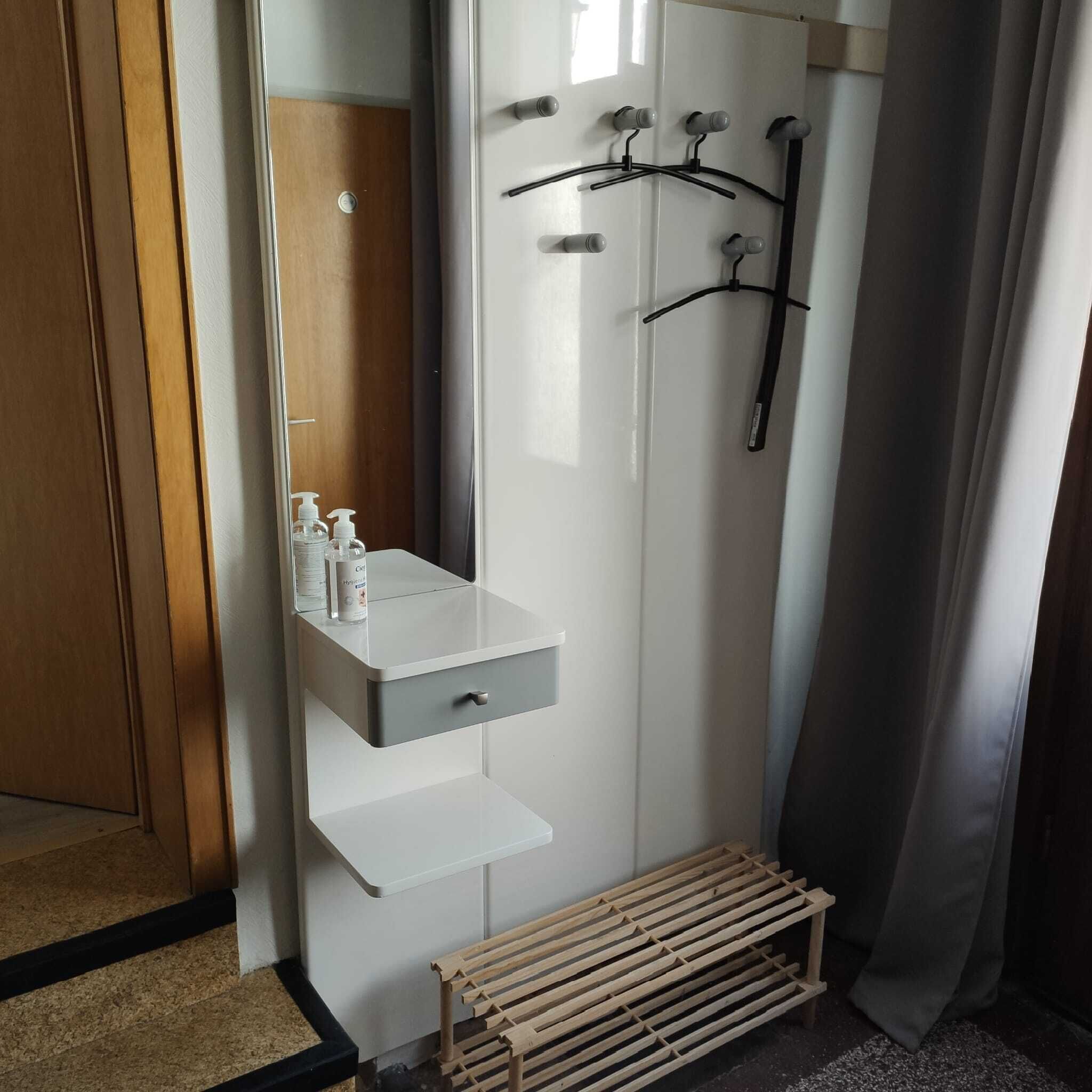 A bathroom with a white vanity, a mirror, a shower with a black hose, and a wooden bench.