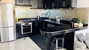 A modern kitchen with dark cabinets, a stainless steel refrigerator, a gas stove, and a black countertop. - Duplex Calme Cosy 5 Minutes du Centre d Essaouira (Essaouira)