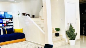 A modern living room with a blue sofa, a white coffee table with a laptop, a staircase, and a flat-screen TV mounted on the wall. - Duplex Calme Cosy 5 Minutes du Centre d Essaouira (Essaouira)