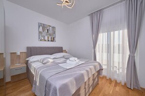 A modern bedroom with a bed, bedside tables, a wall art piece, and a large window with curtains.