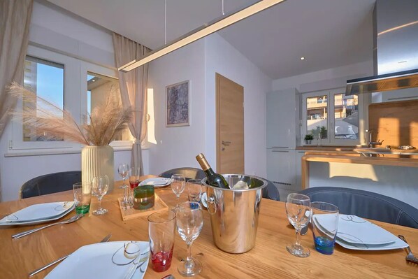 A dining area with a wooden table set for a meal, a bottle of champagne in a metal bucket, and a vase with dried plants.