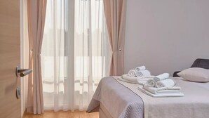 Hotellihuone, jossa on sänky, ovi ja ikkuna, jossa on läpikuultavat verhot.