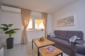 A modern living room with a grey sofa, a wooden coffee table, a potted plant, and a window with curtains.