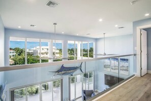 A modern interior with large windows, a balcony, and a view of the ocean and buildings.