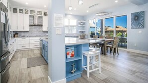 Una cocina moderna con armarios blancos, una isla azul y un comedor con vistas.