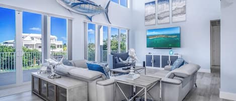 A spacious living room with a large window, a ceiling fan, and a mounted TV.