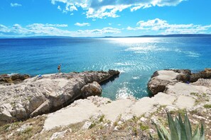 A rocky coastline with clear blue sea and a person standing on the rocks.