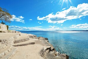 A stone staircase leading to a beach with clear blue water and a bright sky.