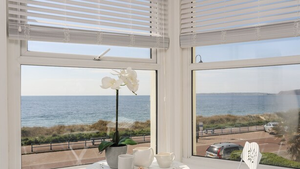 Quarto com vista para o mar, uma mesa com uma planta, uma xícara e um prato de biscoitos.