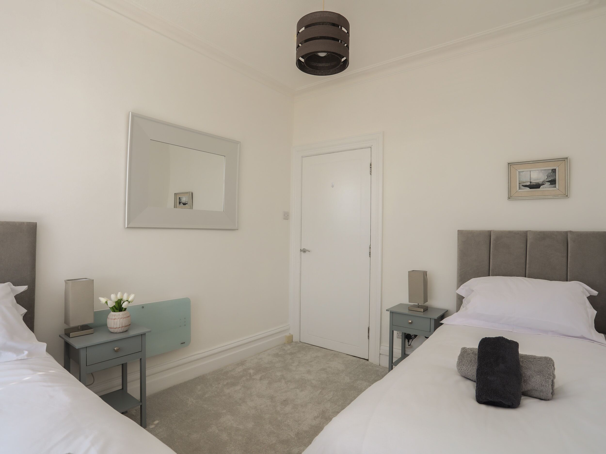 Une chambre d’hôtel avec un lit, des tables de chevet, un miroir, une porte et un tableau au mur.