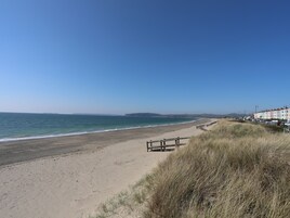 Una playa con una valla de madera, dunas cubiertas de hierba y una hilera de edificios coloridos al fondo.