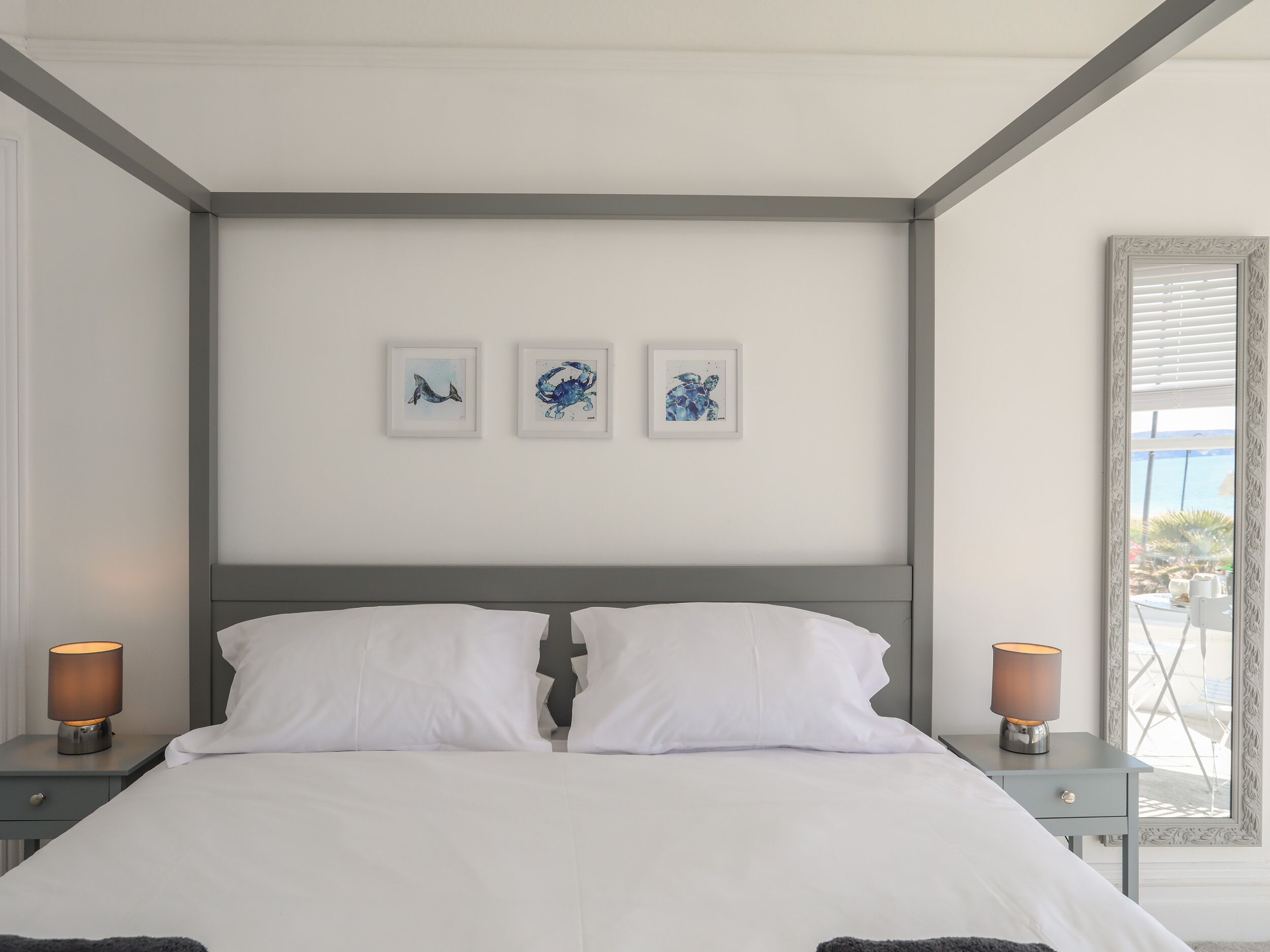 A bedroom with a bed, two bedside tables, and three framed artworks on the wall.