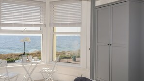 Quarto com vista para o mar, um guarda-roupa branco e um espaço de estar com mesa e cadeiras.