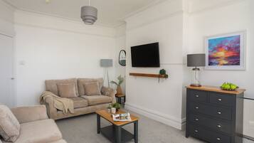 A modern living room with a beige sofa, a coffee table, a TV, a painting, and a dresser.