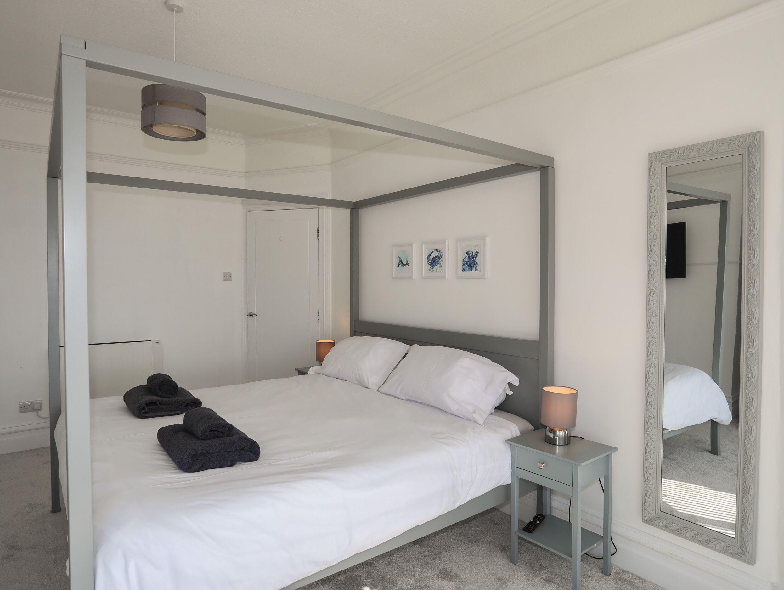 Een moderne slaapkamer met een hemelbed, een nachtkastje met een lamp, een spiegel en kunst aan de muur.