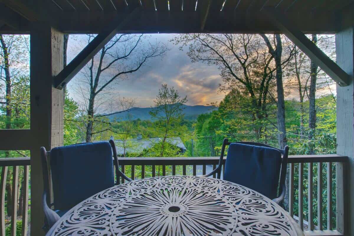 Un espace extérieur abrité, avec une table et des chaises, offrant une vue sur un paysage boisé et des montagnes à l’horizon.