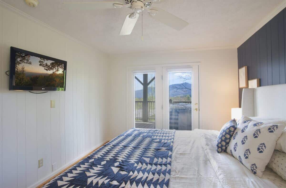 A bedroom with a bed, a ceiling fan, a TV, and a view of the outdoors through a sliding door.