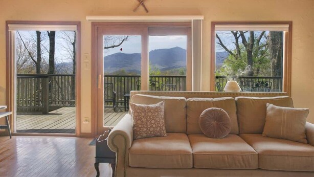 Ein gemütliches Wohnzimmer mit einem beigefarbenen Sofa, einem Holzboden und Blick auf Berge durch große Fenster.