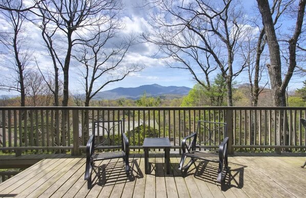 A wooden deck with a table and chairs, overlooking a mountainous landscape.