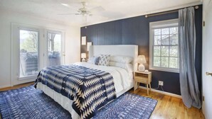 Ein Schlafzimmer mit einem großen Bett, einem Deckenventilator, einem Nachttisch mit Lampe und einem Fenster mit Vorhängen.