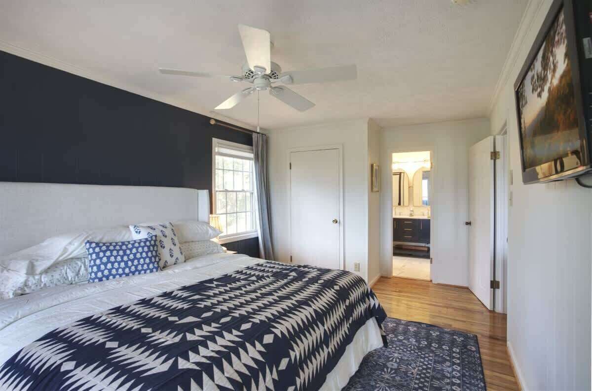 A bedroom with a bed, a ceiling fan, a window, and a door leading to a bathroom.