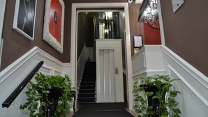 A hallway with a staircase, a red-framed mirror, and two potted plants. - The B Place Ezio (Rome)