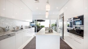 Una cocina moderna con armarios blancos, una isla central y electrodomésticos integrados, incluyendo un horno doble y lavavajillas.