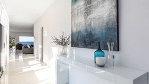 Un pasillo moderno y espacioso con diseño minimalista, que incluye un elegante consola blanca con objetos decorativos y un gran cuadro abstracto en la pared.