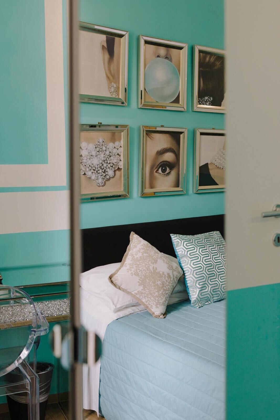 Un dormitorio con paredes color turquesa, una cama con almohadillas estampadas y una pared decorada con marcos.